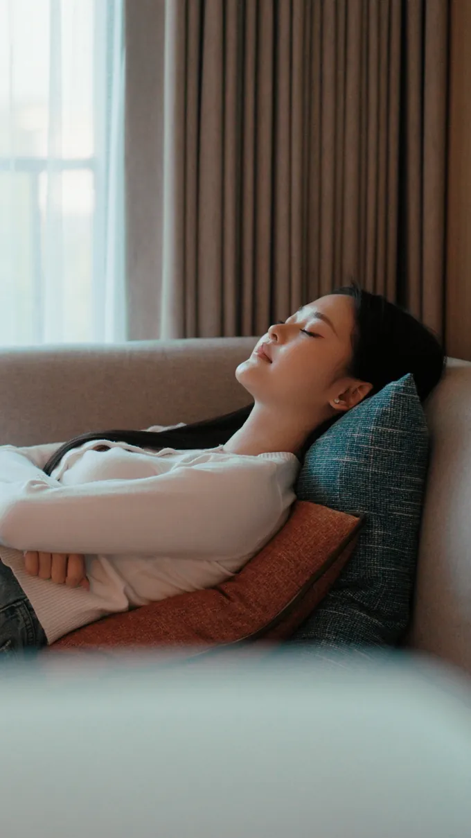 A woman resting back on a sofa with her eyes closed, calm and at ease during a session